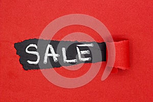 White word SALE on black background on torn red paper.