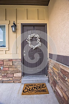 White wreath hanging on gray front door of home with a doormat by the doorstep