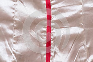 White wrinkled silk fabric as background close up with red zipper in the middle