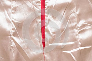 White wrinkled silk fabric as background close up with red zipper in the middle