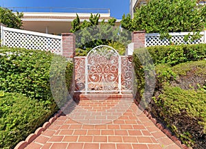 White wrought iron gate of a house with red bricks entrance and walls at La Jolla, California