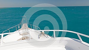 White yacht deck sailing on sea waves on sunny day, close-up. Sea voyage on luxury yacht. Clear blue sky above horizon.