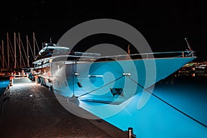 White yacht with a luminous bottom is in the marina at night