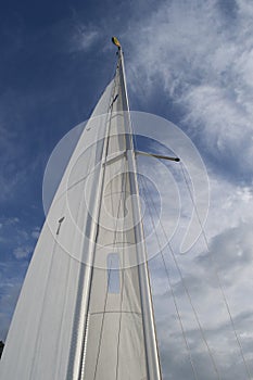 White yacht sail and metal mast against bright blue sky with clouds