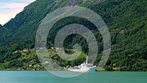 White yacht sailing sailing in Europe with backdrop of homes and forest on side of mountain