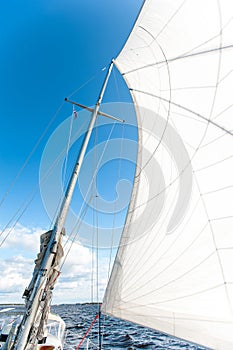 White yacht sails in sunlight on blue cloudy sky background.