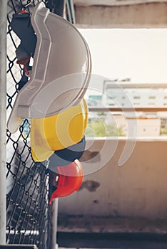 White, yellow, blue and orange helmets that hang on the iron fence at the construction site