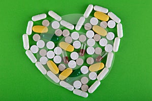 White, yellow, brown pills lay in heart shape on green background. Top view, flat lay