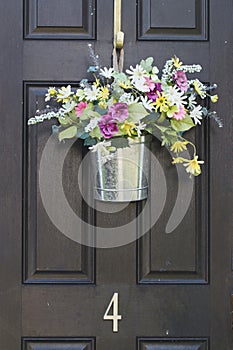 White and yellow daisy flowers in silver metal pail on black door with number 4