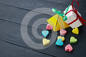 White and yellow gift boxes next to colored sugar hearts on wooden table.