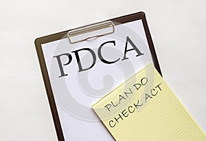 White and yellow paper with text PDCA Plan Do Check Act on a white background with stationery