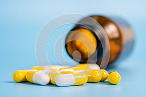 White and yellow pills scattered near opened bottle on blue background. Concept of medical treatment with medicine