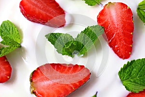 White yoghurt with fresh red juicy strawberry pieces and green mint leaves close up