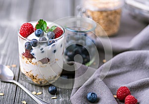 White yogurt in glass jar with raspberries and blueberries on grey napkin