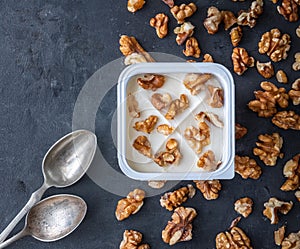 White yogurt in plastic square cup with walnuts with spoons on gray background. Flat view