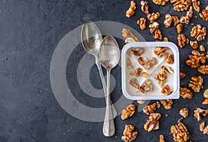 White yogurt in plastic square cup with walnuts with spoons on gray background. Flat view