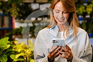 White young florist girl smiling and using cellphone in flower shop