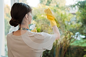 White young woman in gloves washing window with cleaning spay