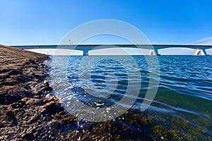 White Zeeland bridge in Holland, blue sea water and sky, sea algae in the foreground. Netherlands