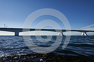 White Zeeland bridge in Holland, blue sea water and sky, sea algae in the foreground. Netherlands