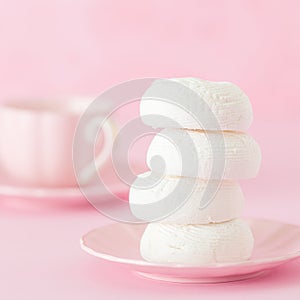 White zephyr dessrt on pink plate, cup of coffee with milk on pastel pink background. Beautiful sweets. Square banner, greeting ca