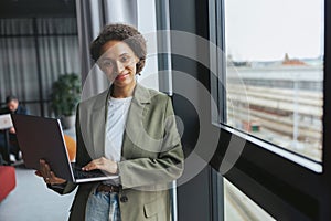 A whitecollar worker in formal wear holds a laptop by a window at a building