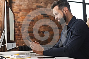 A whitecollar worker is seated at a wooden desk, using a cell phone