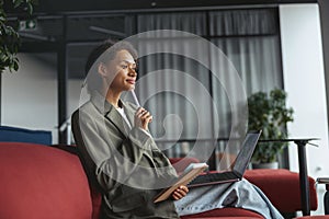 A whitecollar worker is sitting in a room with a laptop and a pen in her mouth