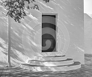Whitewashed traditional church or hermita in a small village in Spain. Shadows cast over circular steps. Monochrome photo