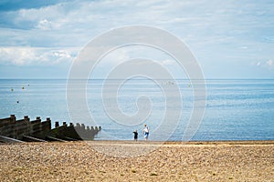 Whitstable beach with a wooden groyne and a woman and small boy at the edge of the water