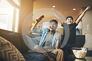 Who better to watch the game with. an enthusiastic father and son watching a sports match on tv at home.