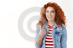 Who me. Gorgeous redhead femenine woman surprised being chosen pointing herself index finger smiling broadly standing