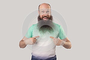 Who? me? Portrait of surprised middle aged bald man with long beard in light green t-shirt standing, pointing himself and looking