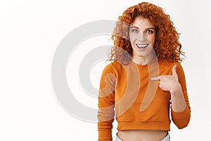 Who me. Surprised redhead girl pointing herself wondering if she is winner, smiling cheerful startled pleasant news