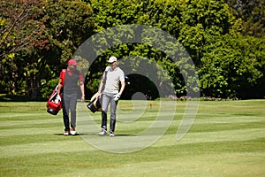 Who needs a caddy with your buddy walking beside you. two men carrying their golf bags across a golf course.