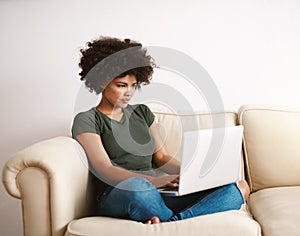 Who needs a office. a woman using her laptop on the sofa at home with her legs crossed.