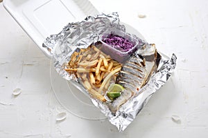 Whole baked seabream, served with potato fries and red cabbage salad, in a takeaway box. Fish and chips lunch set.