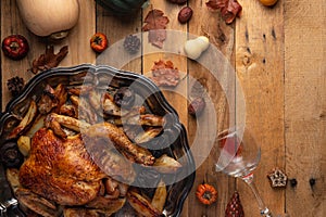 Whole baked turkey stuffed with apples served with potato on the black round dish. Wooden background with autumn decoration.