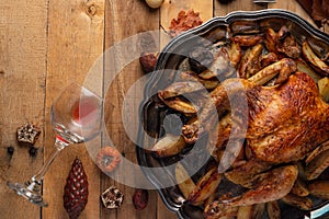 Whole baked turkey stuffed with apples served with potato on the black round dish. Wooden background with autumn decoration.