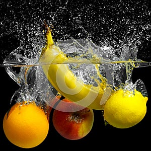 Whole banana, orange, lemon and apple in water on a black background. Fresh fruit with water spray