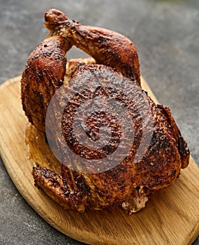 Whole barbecue chicken on a wooden board on a gray background