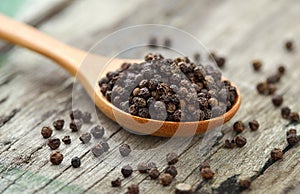 Whole black pepper on wooden spoon