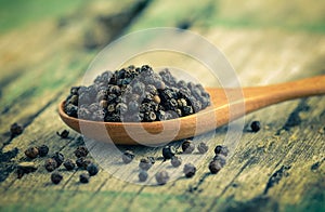 Whole black pepper on wooden spoon