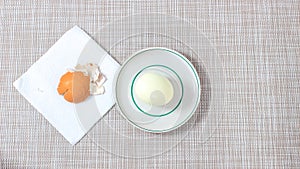 A whole boiled egg on a plate, next to which there is an eggshell