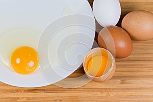 Whole and broken eggs on dish, top view close-up photo