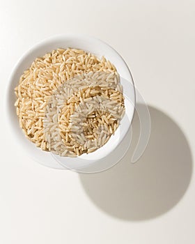 Whole Chinese Rice seed. Grains in a bowl. Shadow over white ta photo