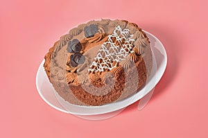 Whole chocolate cake on white round plate on pink background