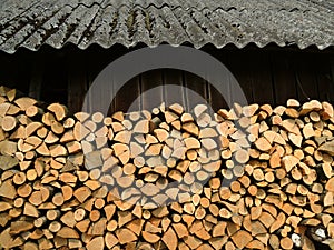 Whole and chopped firewood under overhang near a woodshed stacked for drying