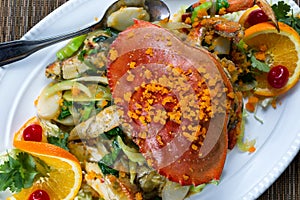 Whole cooked Dungeness crab with cheese and veggies on white serving plate ready to eat