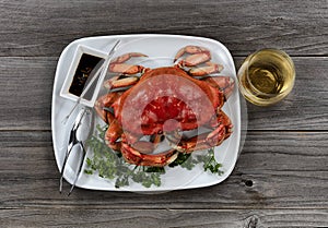 Whole cooked Dungeness crab in dinner table setting with white wine